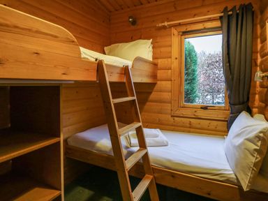 A small wooden bedroom with bunk beds and a window with curtains at Valley View in Rhayader