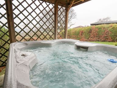 An outdoor hot tub with bubbling water under a wooden lattice structure with trees and bushes in the background at Valley View in Rhayader