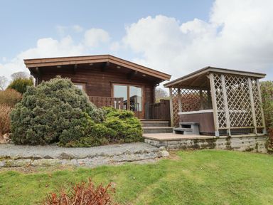 A wooden cabin with a porch and a gazebo on a grassy lawn at Valley View in Rhayader