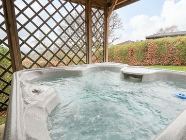An outdoor hot tub under a wooden pergola with lattice walls and a garden hedge in the background at Valley View in Rhayader