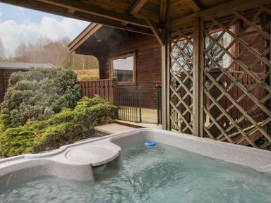 An outdoor hot tub next to a wooden gazebo and a wooden cabin with greenery around at Valley View in Rhayader