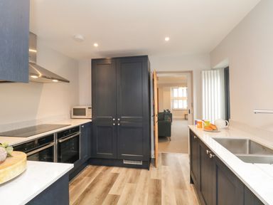 A kitchen with dark cabinets white countertops a stainless steel sink and a view into a living room at Hazelnut Cottage in Windermere