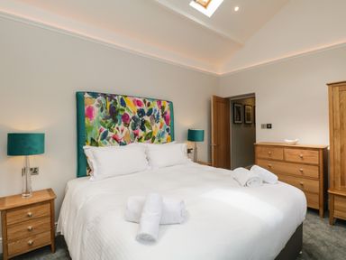A bedroom with a large bed with colorful headboard and towels on the bed at Hazelnut Cottage in Windermere