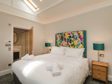 A bedroom with a bed with white linens and colorful headboard two bedside tables with lamps and an open door showing a bathroom at Hazelnut Cottage in Windermere