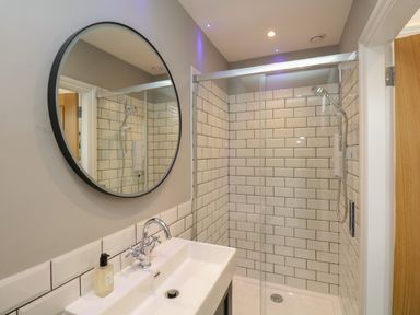 A bathroom with a round mirror above a sink and a shower area with tiled walls at Hazelnut Cottage in Windermere