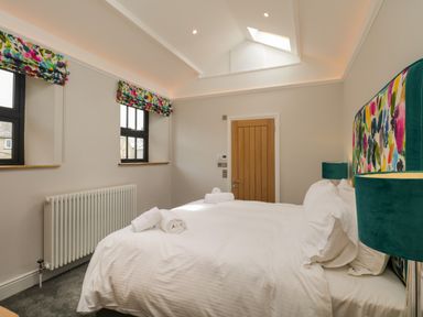 A bedroom with a double bed white bedding colorful headboard two windows with floral blinds and a wooden door at Hazelnut Cottage in Windermere