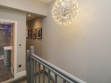 A hallway with gray walls carpeted stairs and a modern spherical light fixture at Hazelnut Cottage in Windermere