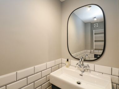 A bathroom sink with a faucet soap dispenser and a mirror above white tiled walls at Hazelnut Cottage in Windermere