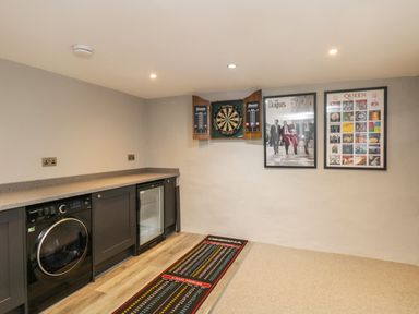 A game room with a dartboard cabinet and dart scoring mat with black cabinets and a washing machine at Hazelnut Cottage in Windermere