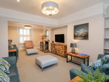 A living room with sofas armchair ottomans a TV and firewood at Hazelnut Cottage in Windermere