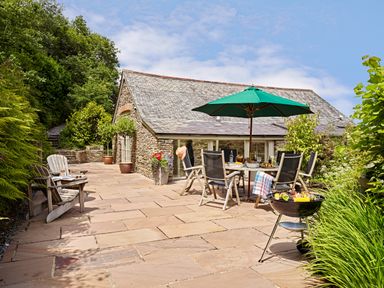 An outdoor patio with chairs table umbrella and barbecue near a stone building at Garden House in Cornworthy