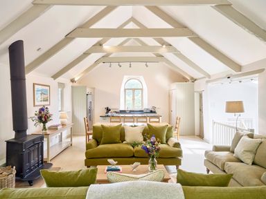 A living room with green sofas wooden table and a black wood stove at Garden House in Cornworthy