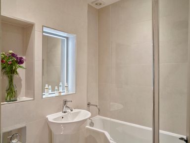 A bathroom with a sink, bathtub with glass partition, built-in shelf with flowers and illuminated mirror at Garden House in Cornworthy