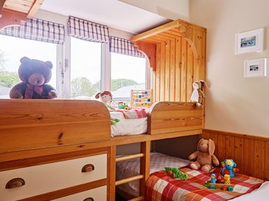 A children's bedroom with a wooden bunk bed toys on the beds and two small framed pictures on the wall at Garden House in Cornworthy