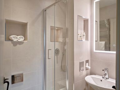 A bathroom with a glass shower enclosure a sink with a faucet and a mirror with built in lighting at Garden House in Cornworthy