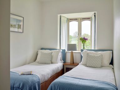 A bedroom with two single beds a lamp and flowers on a window ledge at Garden House in Cornworthy