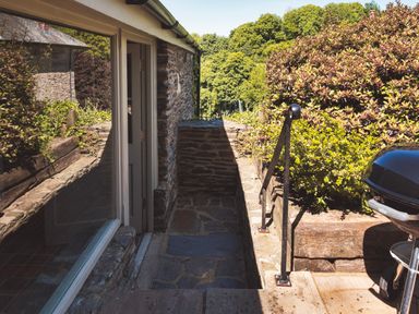 An outdoor stone walkway next to a stone house with plants and a barbecue grill at Garden House in Cornworthy