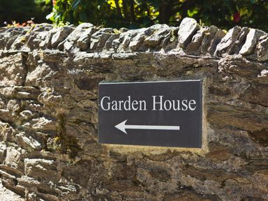 A stone wall with a sign pointing left to Garden House in Cornworthy