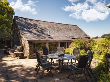 An outdoor patio with a round table and eight chairs next to a stone house with a shingled roof at Garden House in Cornworthy