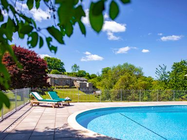 An outdoor swimming pool with two lounge chairs and a stone building in the background at Garden House in Cornworthy