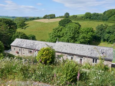 A stone building with a slate roof surrounded by greenery and fields at Haytor Cottage in Cornworthy