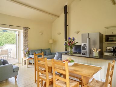 An open kitchen and dining area with wooden table and chairs blue sofas and a stainless steel refrigerator at Haytor Cottage in Cornworthy
