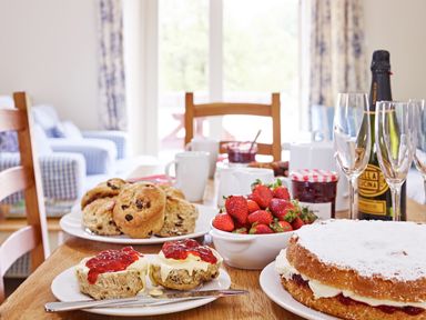 A dining table with scones strawberries jam cake and champagne glasses at Haytor Cottage in Cornworthy