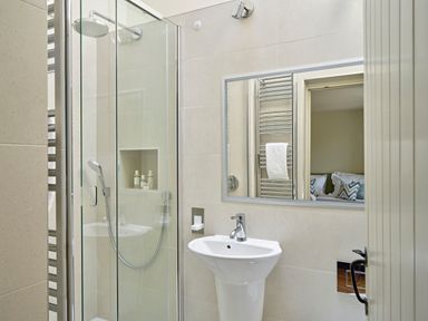 A bathroom with a glass shower enclosure a sink a mirror and a towel rail at Haytor Cottage in Cornworthy