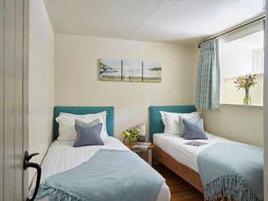 A bedroom with two single beds a small wooden table with a lamp and flowers and a window with curtains at Haytor Cottage in Cornworthy