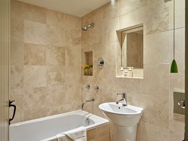 A bathroom with a bathtub shower and sink with toiletries in niches at Haytor Cottage in Cornworthy