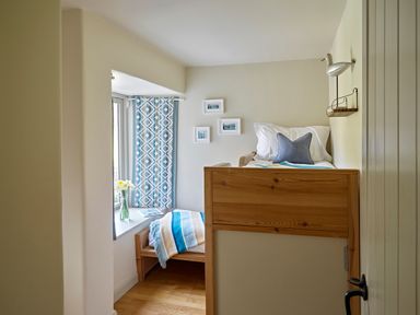 A small bedroom with a bunk bed a window seat with flowers and patterned curtains at Haytor Cottage in Cornworthy