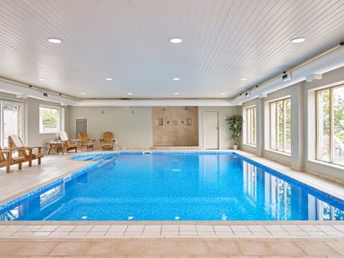An indoor swimming pool with wooden chairs along the side and large windows at Haytor Cottage in Cornworthy