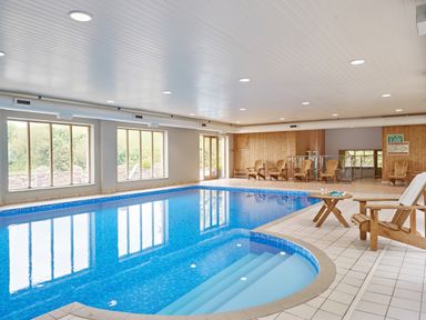An indoor swimming pool with wooden chairs and large windows at Haytor Cottage in Cornworthy