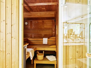 A wooden sauna room with benches towels a wooden bucket and ladle visible through a glass door at Haytor Cottage in Cornworthy