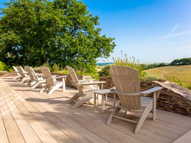 A row of Adirondack chairs on a wooden deck overlooking fields and trees at Haytor Cottage in Cornworthy