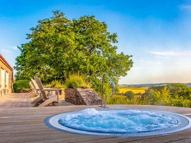 An outdoor wooden deck with a bubbling hot tub chairs and large tree with a countryside view at Haytor Cottage in Cornworthy