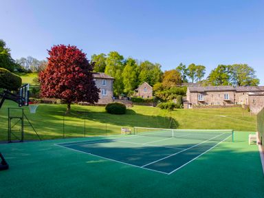 An outdoor tennis court with benches and a basketball hoop near stone buildings and trees at Haytor Cottage in Cornworthy
