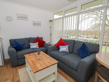 A sitting area with two gray sofas with colored cushions a wooden coffee table and large windows with blinds at Pebbles in Cromer