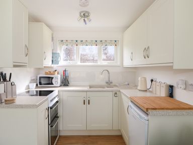 A kitchen with white cabinets and countertops a sink stove microwave and various kitchen utensils at Pebbles in Cromer
