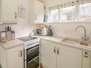 A kitchen with stove microwave sink utensils and cabinets at Pebbles in Cromer