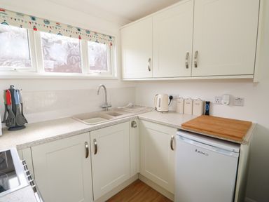 A kitchen with white cabinets a double sink a kettle three labeled containers a cutting board and kitchen utensils on the countertop at Pebbles in Cromer
