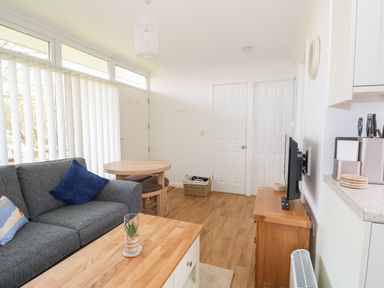 A living room with a gray sofa and round dining table near vertical window blinds at Pebbles in Cromer