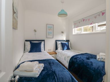 A bedroom with two single beds blue cushions and folded towels on the beds at Pebbles in Cromer