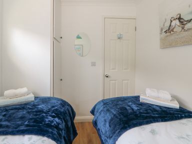 A bedroom with two single beds covered with blue blankets and folded towels on top at Pebbles in Cromer