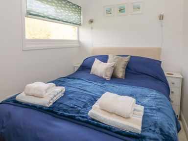 A bedroom with a bed covered in blue bedding two bedside tables and a window with a patterned blind at Pebbles Cromer