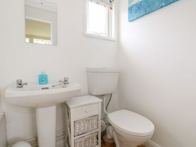 A small bathroom with a white toilet and pedestal sink with blue soap and a cabinet with baskets at Pebbles in Cromer
