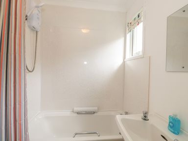A bathroom with a bathtub a shower curtain a shower head a sink and a window at Pebbles in Cromer
