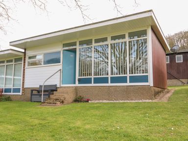 The exterior of a modern house with large windows a blue door and steps leading to a bench on a grassy lawn at Pebbles in Cromer