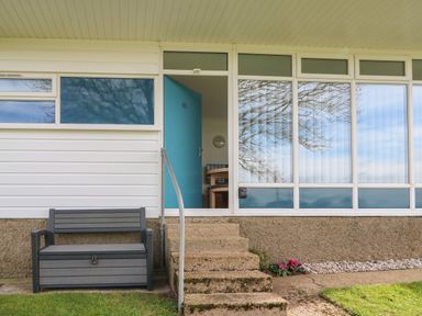 Exterior of a building with a blue door number 63 steps leading up and a bench at Pebbles in Cromer