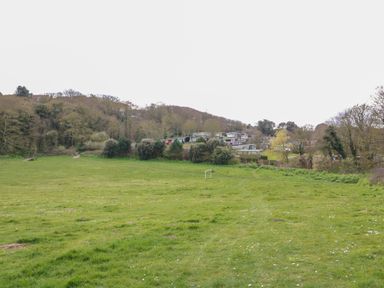 A grassy field with a small soccer goal surrounded by trees and houses in the background at Pebbles Cromer